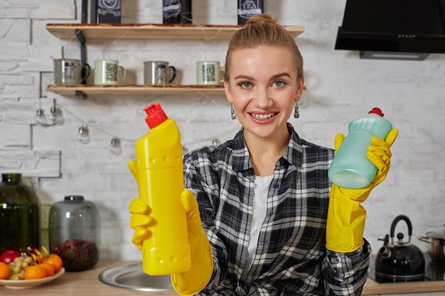 Donna che confronta i prodotti detergenti, tiene in mano due bottiglie e le controlla nella cucina di casa.