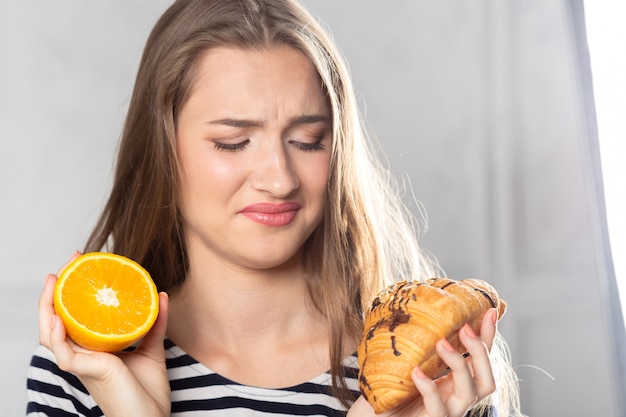 Donna che confronta torta malsana e frutta arancione