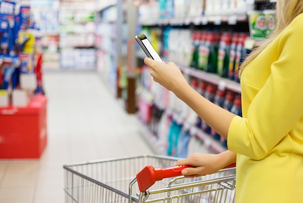 Donna che controlla la lista della spesa sul suo smartphone al supermercato