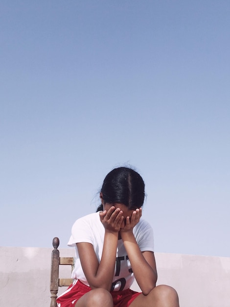 Donna che copre il viso con le mani mentre è seduta sulla sedia.
