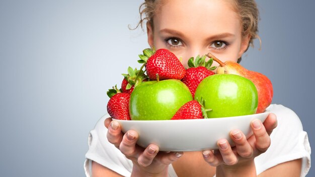 Donna che copre il viso con una ciotola di fragole e mele