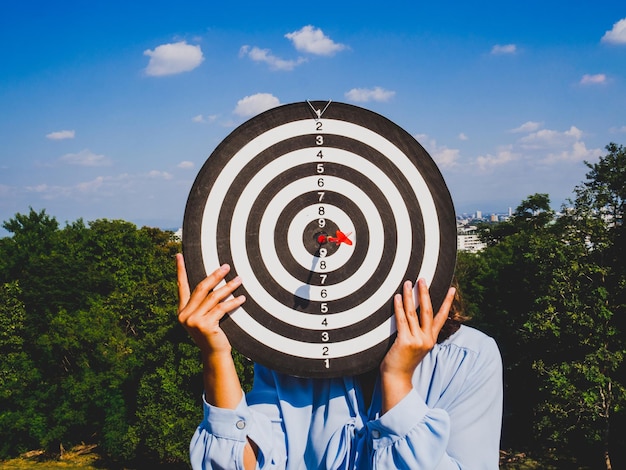 Donna che copre la faccia con una dartboard contro il cielo