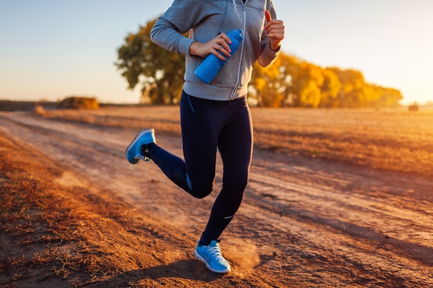 Donna che corre nel campo autunnale al tramonto. Concetto di stile di vita sano. Persone sportive attive. Primo piano delle gambe