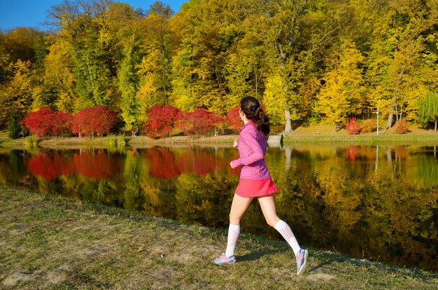 Donna che corre nel parco di autunno, bello corridore della ragazza che pareggia all'aperto, preparandosi per la maratona, esercitandosi e concetto di forma fisica