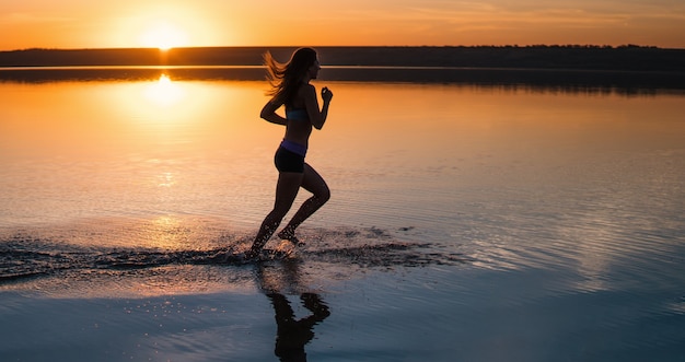 Donna che corre sulla spiaggia al tramonto.