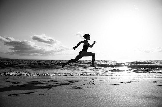 Donna che corre sulla spiaggia bella ragazza in abiti sportivi che corre sul mare