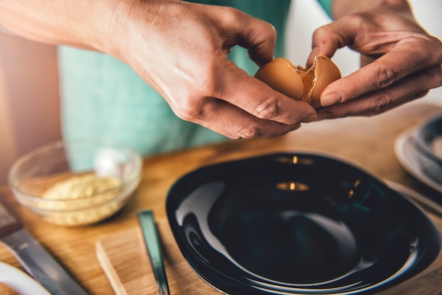 Donna che cucina e che rompe le uova nel piatto