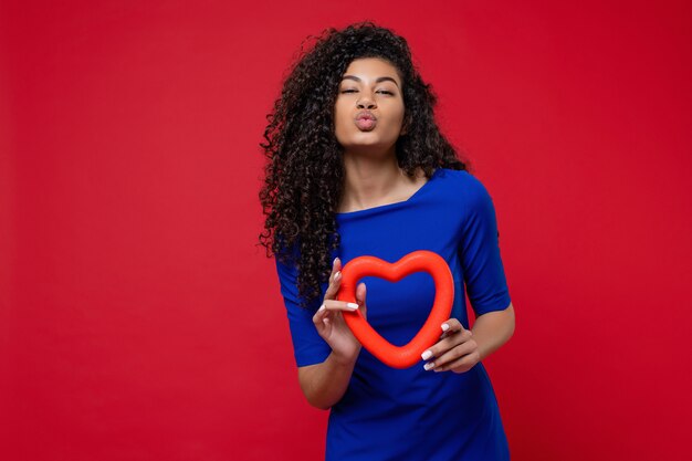 Donna che dà bacio smooch con vestito da portare a forma di cuore sulla parete rossa