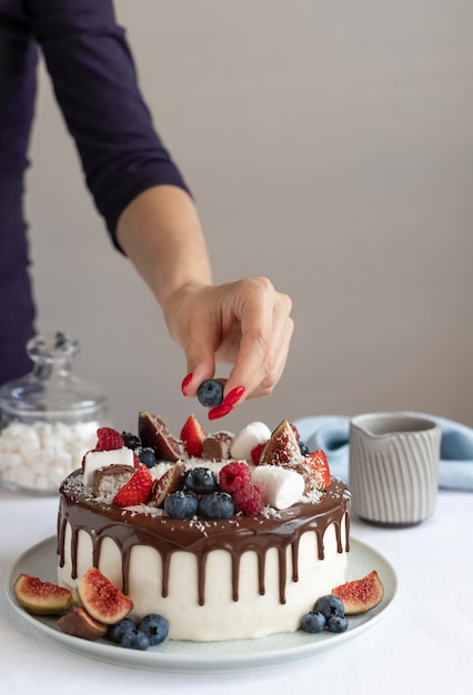 Donna che decora la torta di compleanno con frutti di bosco freschi deliziosi dolci fatti in casa al forno dessert