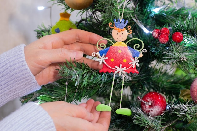 Donna che decora un albero di Natale a casa, primo piano delle mani che appendono un ornamento fatato