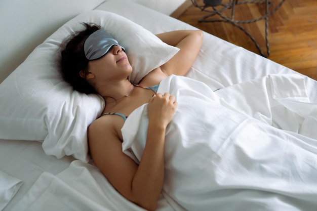 Donna che dorme nella maschera per dormire a letto con lenzuola bianche