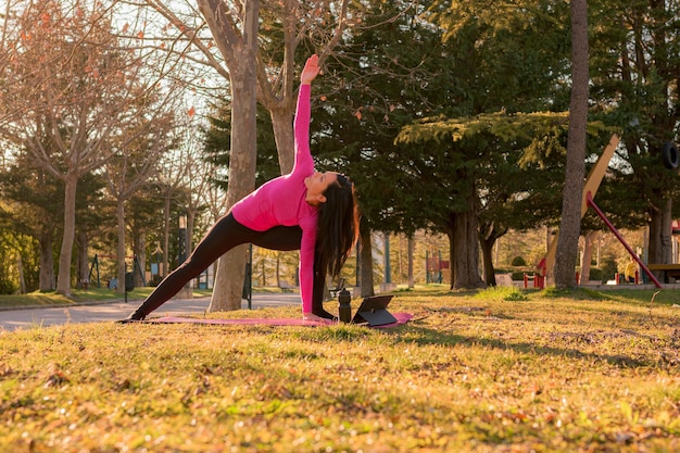 Donna che esegue esercizi di yoga in un parco al tramonto