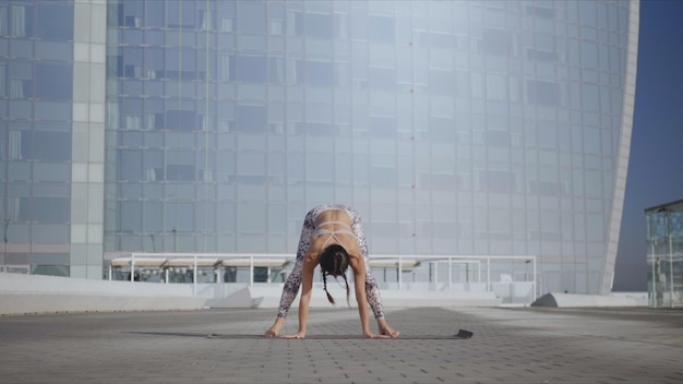 Donna che esegue yoga in strada urbana Signora che fa la posa della ghirlanda sul tappeto all'aperto