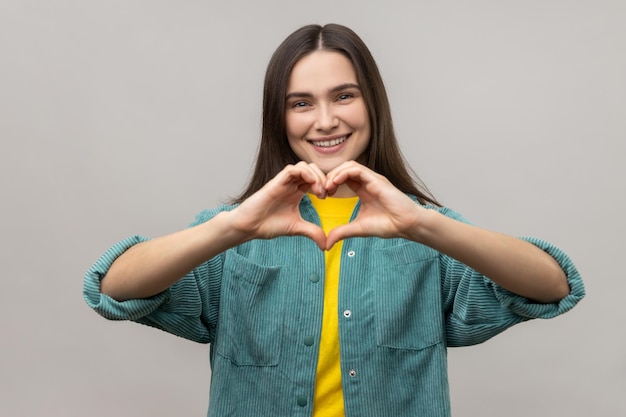 Donna che fa a forma di cuore con le mani e sorride amichevole alla telecamera che mostra il simbolo di amore e cura