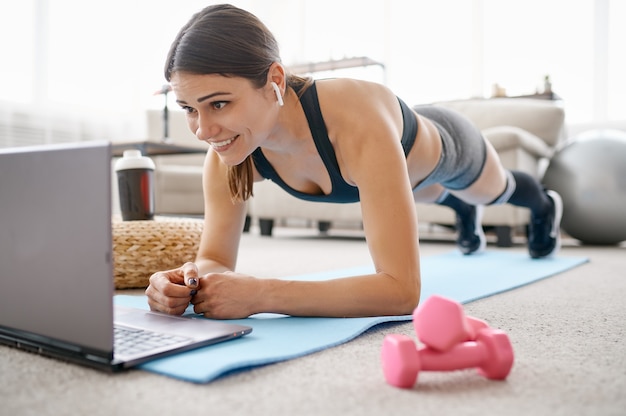 Donna che fa esercizio di addominali, formazione online in forma al computer portatile. Persona di sesso femminile in abbigliamento sportivo, allenamento sportivo internet, interno della stanza