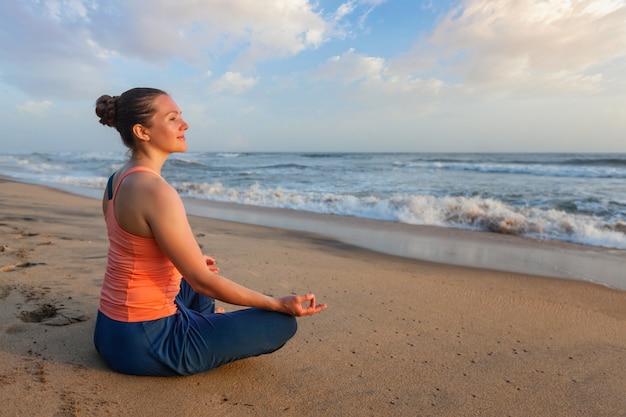 Donna che fa i oudoors di yoga alla spiaggia - posa del loto di Padmasana