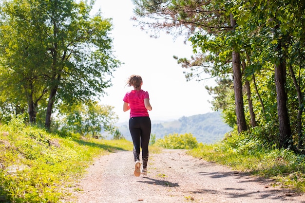 donna che fa jogging su una strada di campagna attraverso la bella foresta soleggiata, l'esercizio fisico e il concetto di fitness