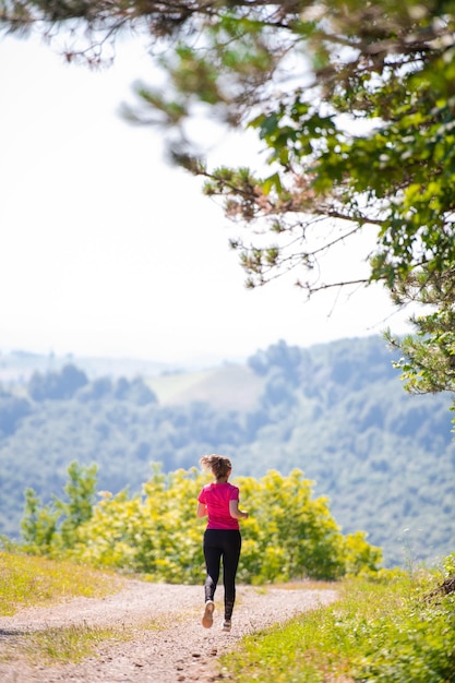 donna che fa jogging su una strada di campagna attraverso la bella foresta soleggiata, l'esercizio fisico e il concetto di fitness