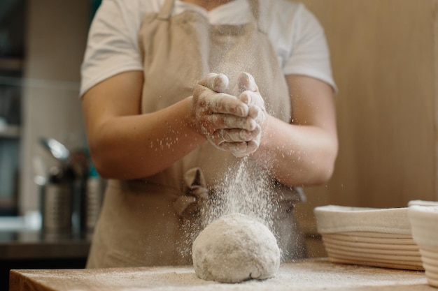 Donna che fa l'impasto del pane francese fatto in casa Cospargendo la farina sull'impasto che si trova su un piano di lavoro