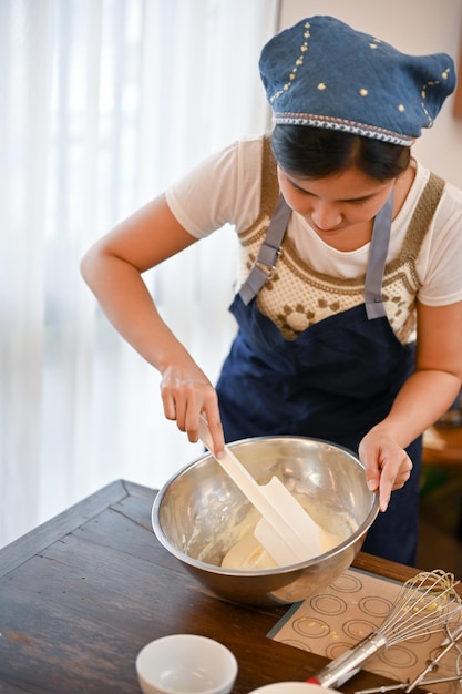 Donna che fa l'ingrediente di miscelazione del bigné nella ciotola con la spatola in cucina