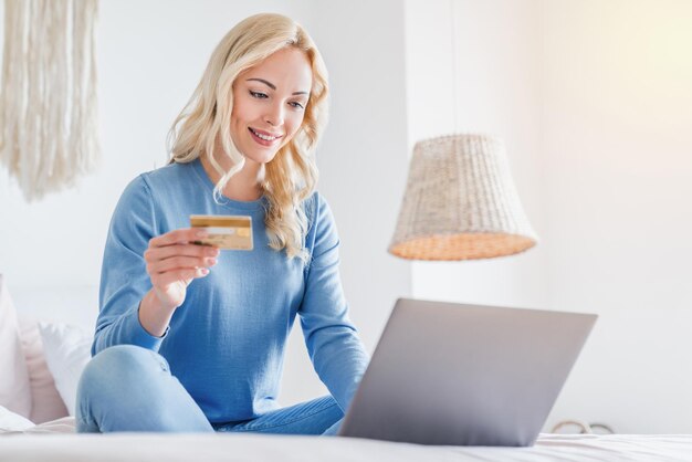 Donna che fa shopping online utilizzando laptop e carta di credito mentre si siede sul letto a casa