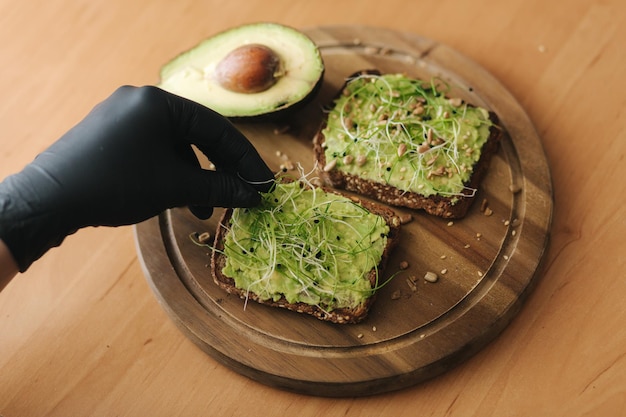 Donna che fa un panino vegano con pane di segale tostato con guacamole e micro verdure Donna cospargere con semi di sesamo sul panino