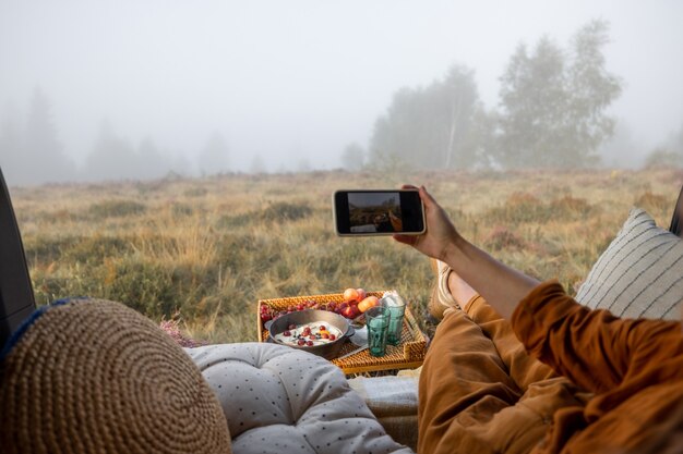 Donna che fa un picnic e si gode una splendida vista sulla natura in caso di nebbia, seduta rilassata nel bagagliaio del veicolo, vista dall'interno di un'auto