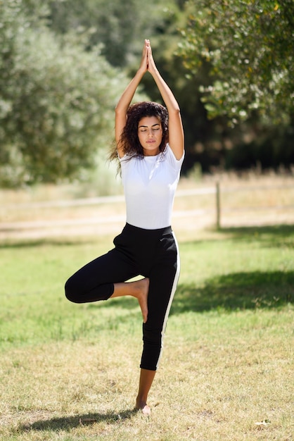 Donna che fa yoga sul campo contro gli alberi