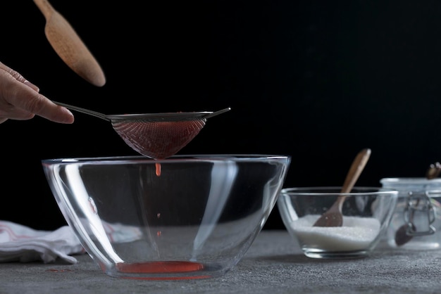 Donna che filtra la marmellata di fragole attraverso un setaccio cucina casalinga e concetto di cucina