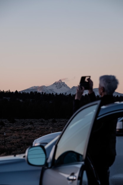 Donna che fotografia mentre è in piedi accanto all'auto contro il cielo durante il tramonto