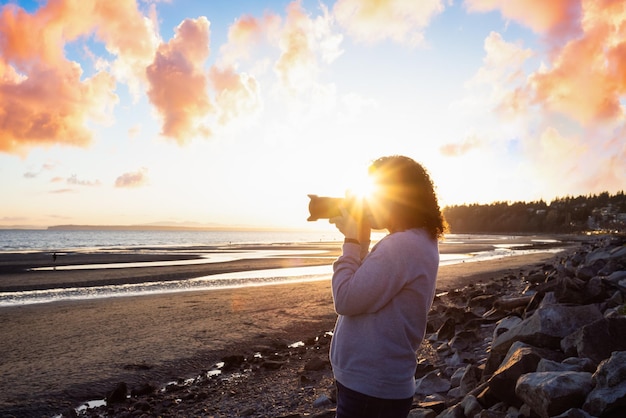 Donna che fotografia sulla spiaggia contro il cielo durante il tramonto