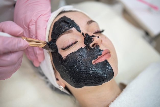 donna che giace male in una clinica termale e riceve una maschera cosmetica nera crema concetto di cura del corpo per la pelle pulita