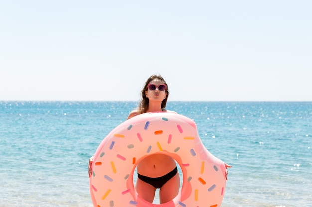 Donna che gioca con anello gonfiabile. Ragazza che si rilassa sul gonfiabile rosa sulla spiaggia. Vacanze estive e concetto di vacanza su un'isola tropicale.