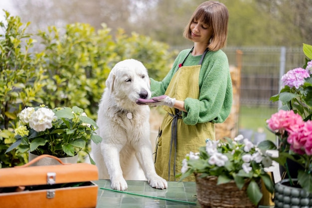 Donna che gioca con il suo cane bianco mentre si prende cura dei fiori in giardino