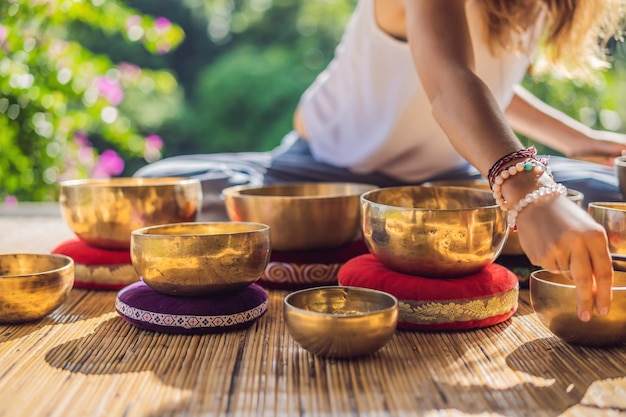 Donna che gioca su una ciotola tibetana mentre è seduto su una stuoia di yoga contro una cascata Tonnellata d'epoca Bella ragazza con perline di mala meditando