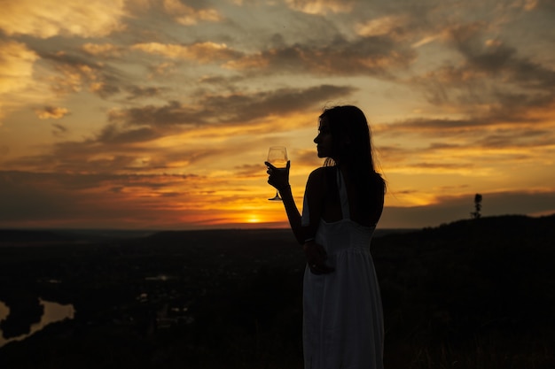 Donna che gode del tramonto con un bicchiere di vino bianco.
