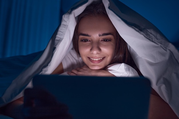 Donna che guarda film sul tablet sotto la coperta