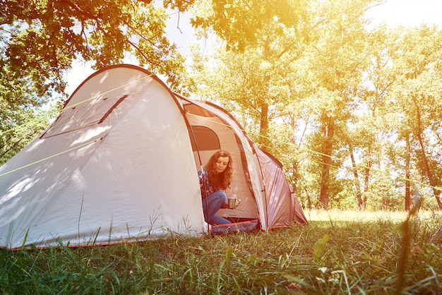 Donna che guarda fuori dalla tenda turistica sulla mattina di sole nella foresta