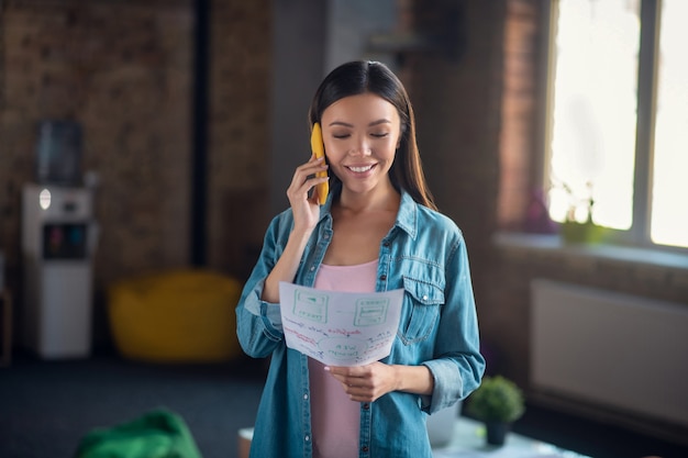 Donna che guarda i suoi appunti mentre parla al telefono