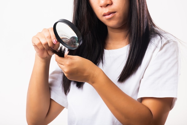 Donna che guarda i suoi capelli distrutti con lente d'ingrandimento