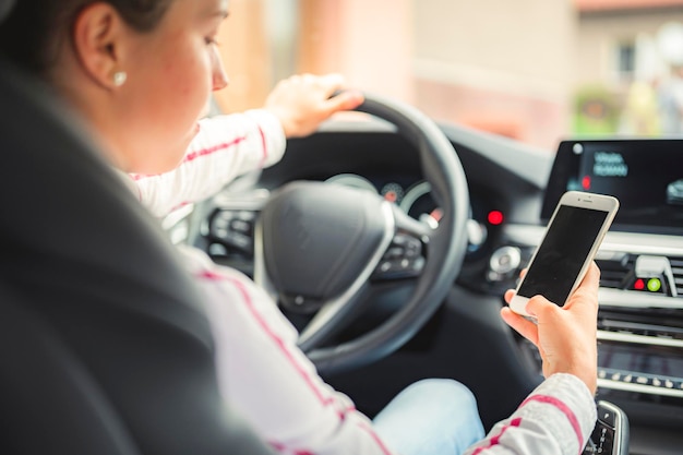 Donna che guarda il telefono cellulare durante la guida di un'auto Autista che utilizza uno smartphone in auto