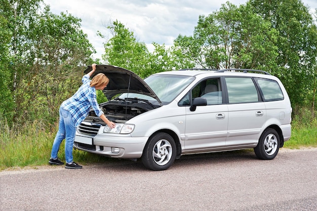 Donna che guarda sotto il cofano di un'auto rotta