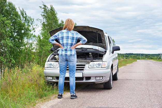 Donna che guarda sotto il cofano di un'auto rotta