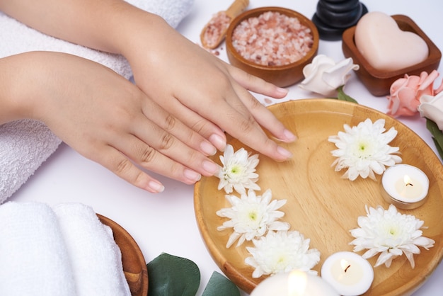 Donna che immerge le mani in una ciotola di acqua e fiori, trattamento Spa e prodotto per piedi femminili e spa per le mani, massaggio con ciottoli, acqua profumata di fiori e candele, relax. Lay piatto. vista dall'alto.