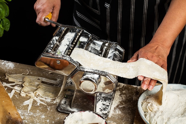 Donna che impasta la pasta con una macchina per la pasta su un tavolo di legno