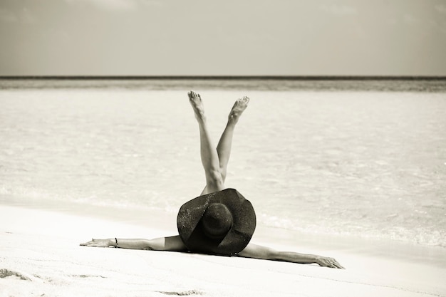 Donna che indossa cappello sulla sabbia con le gambe alzate, bellissima foto sulla spiaggia delle Maldive