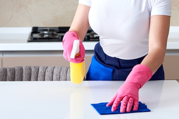 Donna che indossa guanti di gomma tavolo pulizia con un panno. Disinfezione di un tavolo da cucina con candeggina