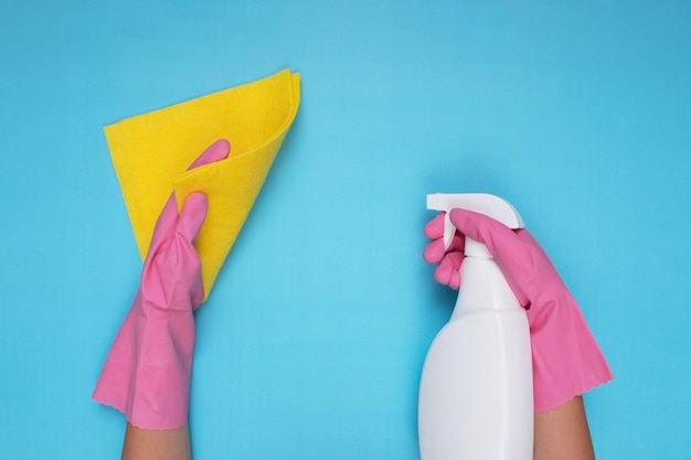 Donna che indossa guanti per la pulizia rosa su sfondo azzurro con in mano uno spray detergente e un panno per la pulizia