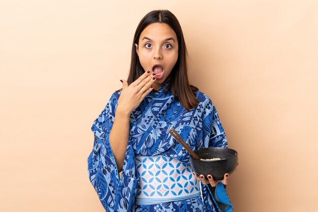 Donna che indossa kimono e che tiene una ciotola piena di noodles che tiene una ciotola di noodles con le bacchette e sorpreso