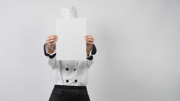 Donna che indossa l'uniforme da chef e tiene in mano carta A4 bianca su sfondo bianco.